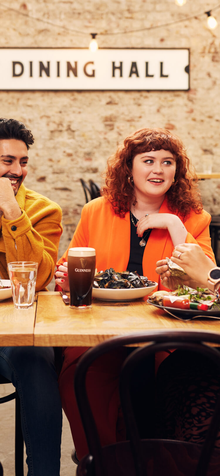 Group of friends laughing and enjoying their meal at the Brewers’ Dining Hall, one with the pairing of mussels & Guinness and another with hake & Hop House 13.